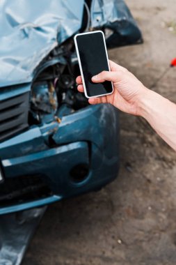 hasarlı arabanın yanında boş ekranlı akıllı telefonu tutan adamın seçici odağı 