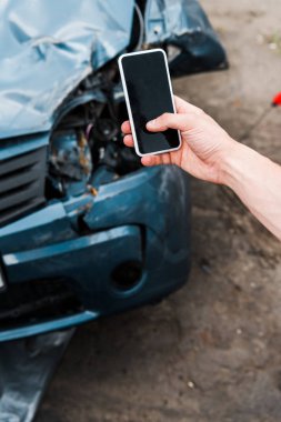 selective focus of man holding smartphone with blank screen near damaged car  clipart