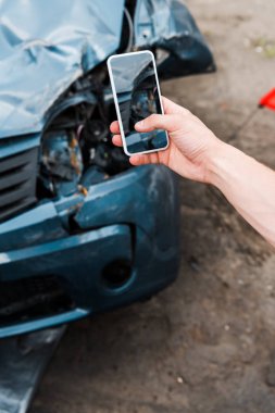 cropped view of man holding smartphone with blank screen near damaged car  clipart