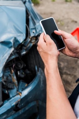 kaza yapılan arabanın yanında boş ekranlı akıllı telefonu tutan adamın kırpılmış görünümü 