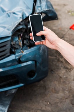 kaza yapılan arabanın yanında boş ekranlı akıllı telefonu tutan adamın seçici odağı 