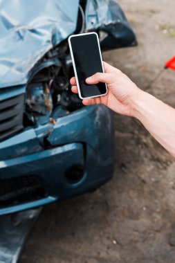 selective focus of man holding smartphone with blank screen near crashed car  clipart