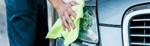 панорамный снимок мойки автомобиля с зеленой тряпкой и чистящей фарой автомобиля
