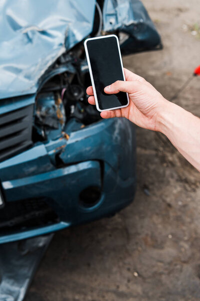 selective focus of man holding smartphone with blank screen near damaged car 