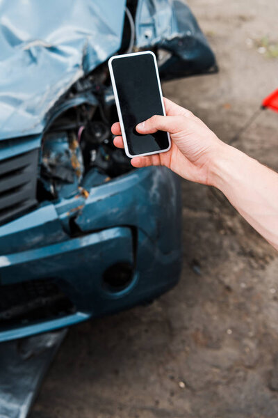 selective focus of man holding smartphone with blank screen near crashed car 