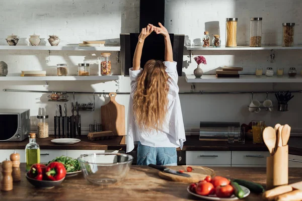 年轻女子在厨房里举手站在白衬衫的背面 — 图库照片