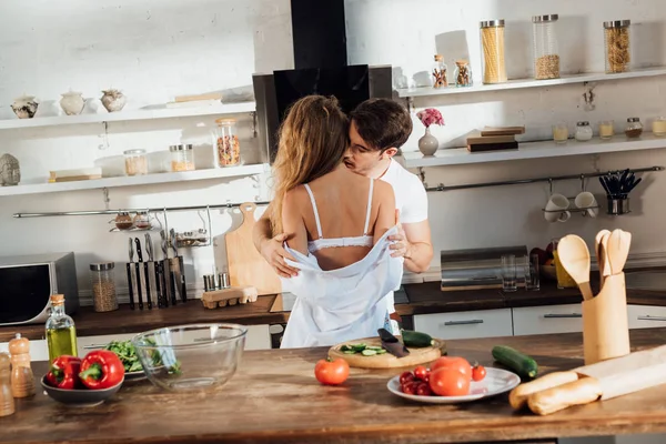 男は服を脱いで キッチンで野菜とテーブルの近くにセクシーなガールフレンドにキス — ストック写真