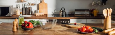 panoramic shot of fresh vegetables and cooking utensils on table in kitchen clipart