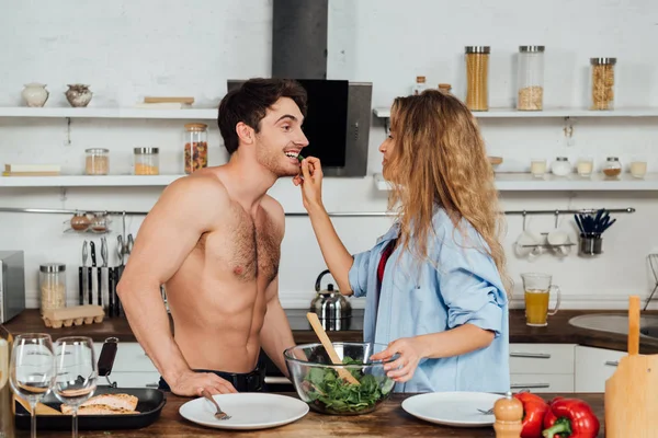 Chica Alimentación Sin Camisa Novio Con Ensalada Cocina — Foto de Stock