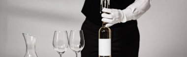 panoramic shot of waiter in white glove opening bottle of wine in restaurant clipart