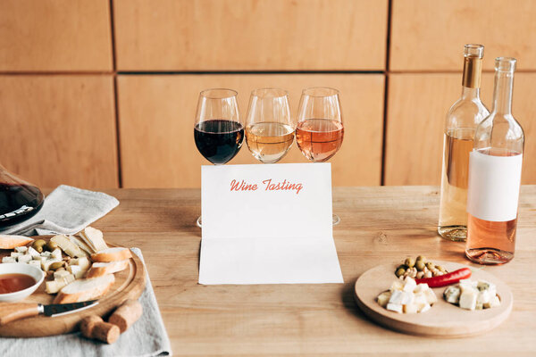 wine glasses, bottles, wine tasting document and food on wooden table