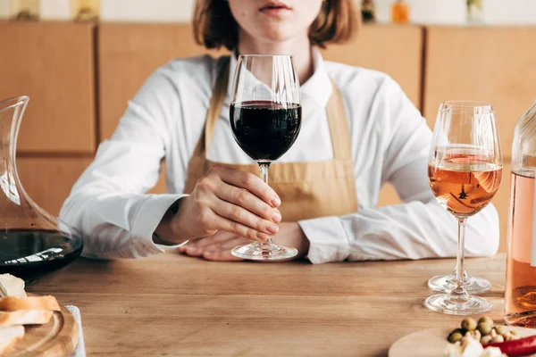 Vista Cortada Sommelier Avental Segurando Copo Vinho Enquanto Sentado Mesa — Fotografia de Stock