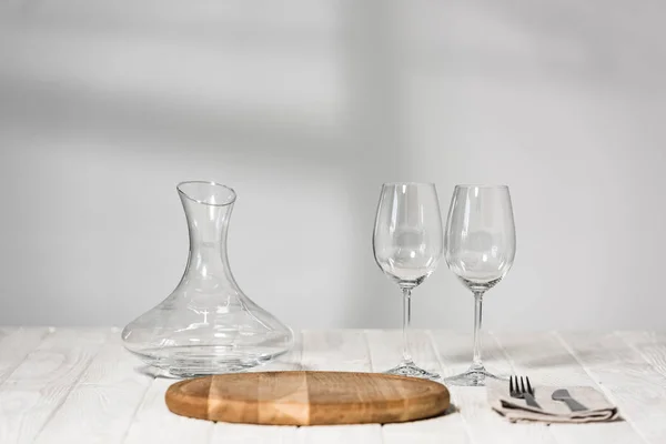 jug, wine glasses, cutlery and cutting board on wooden surface in restaurant