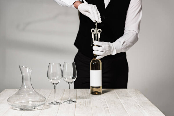 частичный вид официанта в белых перчатках, открывающего бутылку вина штопором
