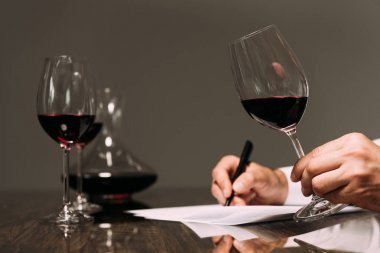 partial view of sommelier writing at table and holding wine glass  clipart