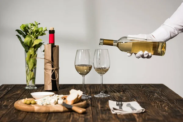 cropped view of waiter in white glove pouring wine in wine glasses