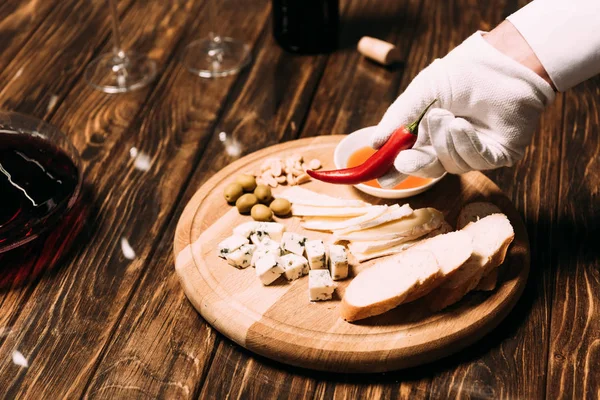 cropped view of waiter in white glove holding pepper near table with food and wine