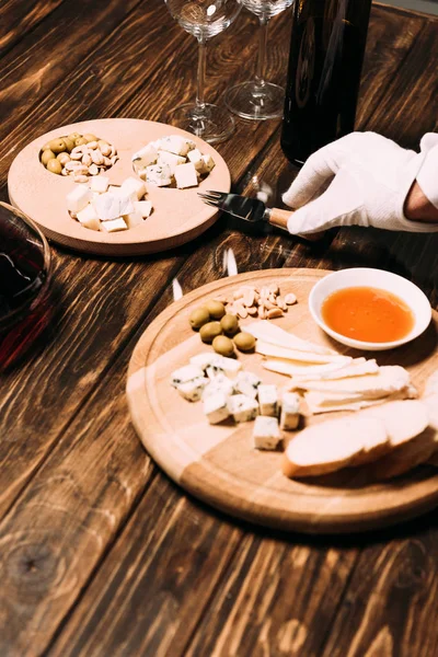 cropped view of waiter in white glove near table with food and wine