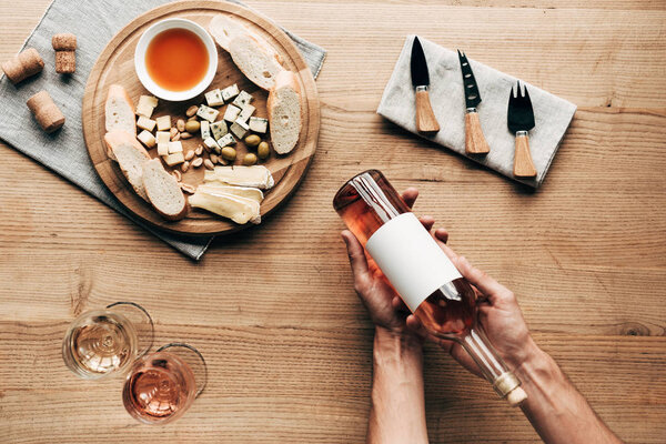 partial view of sommelier holding bottle of wine at table with wine glasses, food and cutlery