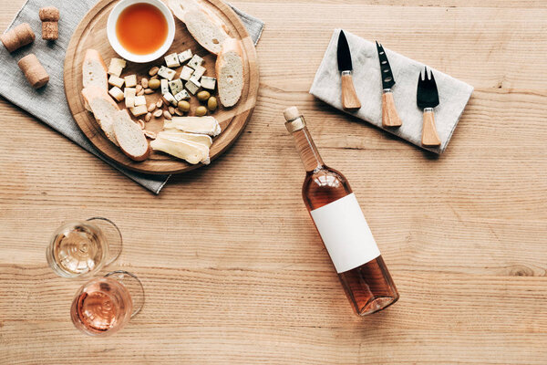 top view of wine glasses, bottle of wine, sauce, bread, cheese, olives, corks and cooking utensils on wooden surface