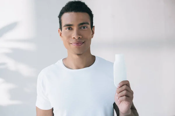 Młody Mężczyzna Trzyma Białą Butelkę Kosmetykiem Krem Patrząc Kamerę — Zdjęcie stockowe