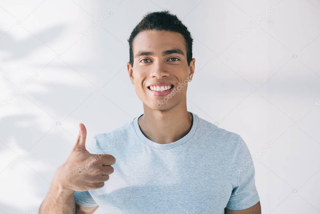 handsome man showing thumb up, smiling and looking at camera