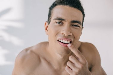 portrait shot of muscular mixed race  man touching teeth while looking at camera clipart