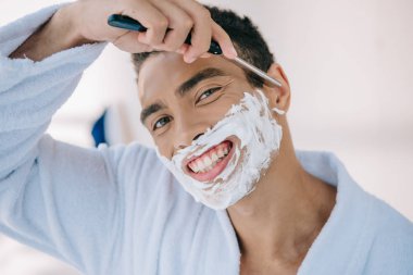 güzel adamın portre çekimi, bornozlu, tıraş bıçağı ile yüz, gülümseyen ve kameraya bakıyor