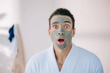 yüz üzerinde kil maskesi ile şok adam kamera bakıyor