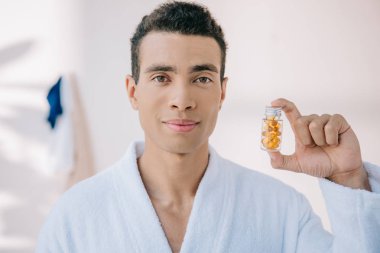 bornoz yakışıklı adam vitamin ile şişe tutan ve kameraya bakarak