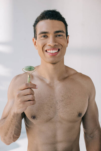 Красивый мускулистый смешанный расовый мужчина представляет каменный нефритовый ролик и улыбается, глядя в камеру
