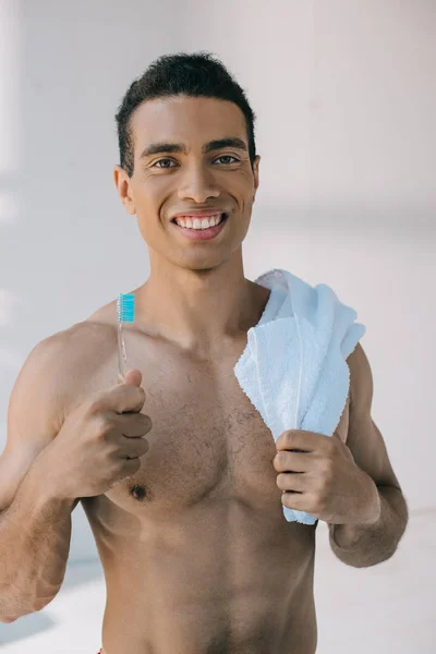 青いタオルを肩に抱え カメラを見ながら歯ブラシを持つ筋肉混合レースの男 — ストック写真
