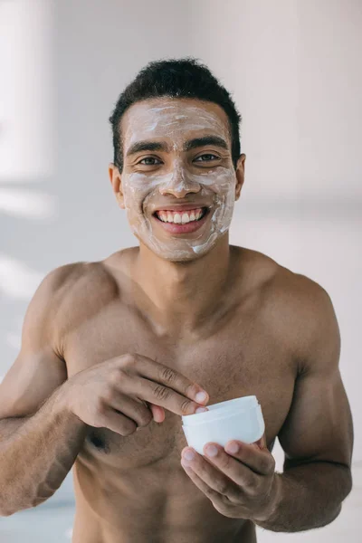 肌肉混合种族男子与奶油在脸上采取化妆品奶油与手指从容器 而看着相机 — 图库照片