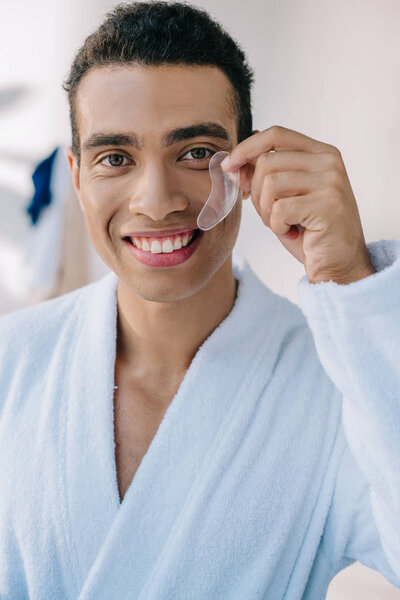 handsome young man in bathrobe showing patch and smiling while looking at camera