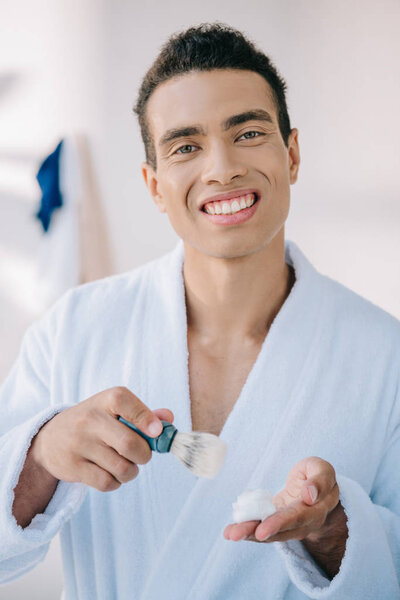 handsome man with shaving brush and shaving cream smiling and looking at camera