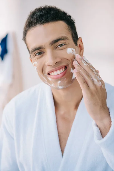 Jovem Bonito Roupão Aplicando Espuma Facial Sorrindo Enquanto Olha Para — Fotografia de Stock