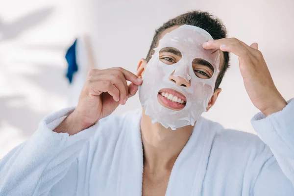 Young Man Bathrobe Trying Take Face Mask While Looking Camera — Stock Photo, Image
