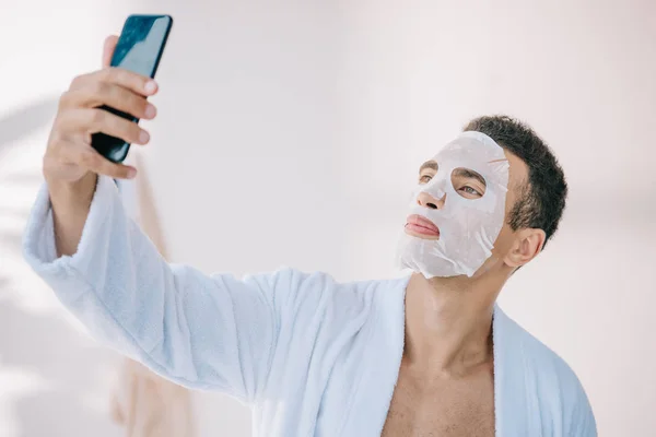 Fiatal Férfi Fürdőköpeny Kozmetikai Maszk Arcon Figyelembe Selfie Okostelefonon — Stock Fotó