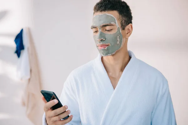 Homem Bonito Com Máscara Barro Rosto Robe Segurando Smartphone — Fotografia de Stock