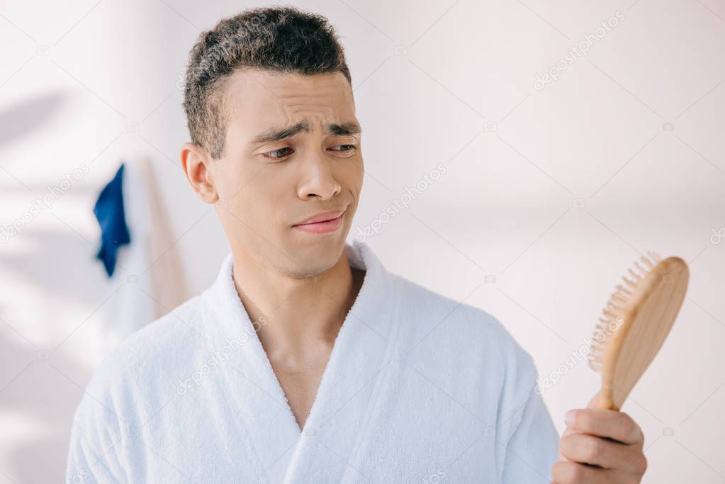 disappointed young man in bathrobe holding hairbrush 
