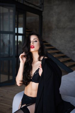  kanepe üzerinde otururken ve kamera bakarak siyah iç çamaşırı seksi kız ceket tutarak