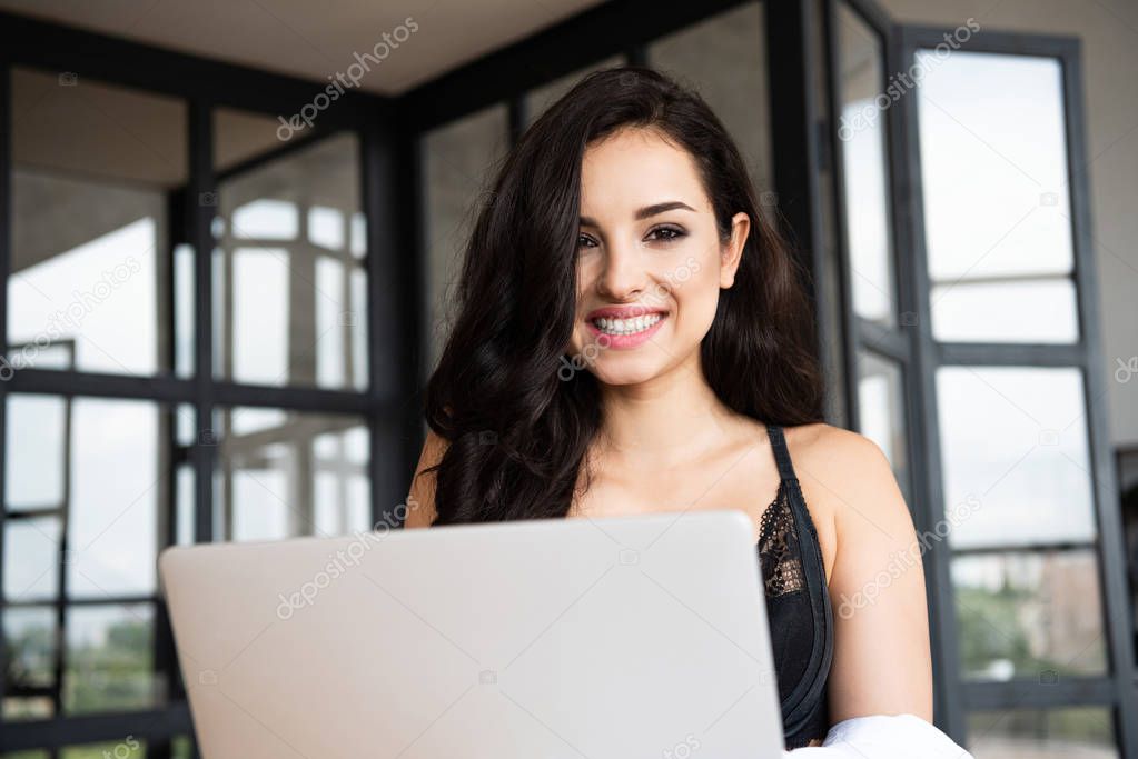 sexy girl in black underwear and white shirt using laptop while smiling and looking at camera