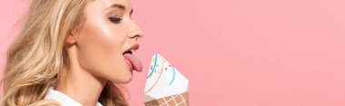 side view of beautiful sexy blonde woman in white faux fur jacket licking decorative ice cream isolated on pink, panoramic shot clipart