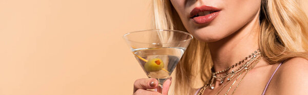 cropped view of elegant blonde woman in necklace holding cocktail isolated on beige, panoramic shot