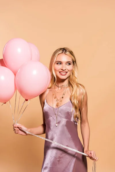 幸福优雅的金发女郎在紫色的色服礼服和项链拿着粉红色的气球米色 — 图库照片
