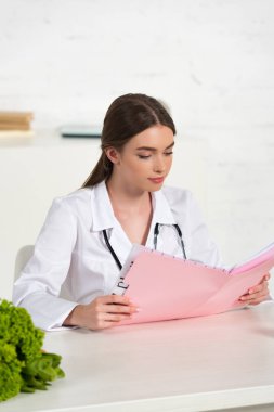 işyerinde beyaz ceket okuma klasöründe odaklanmış diyetisyen 