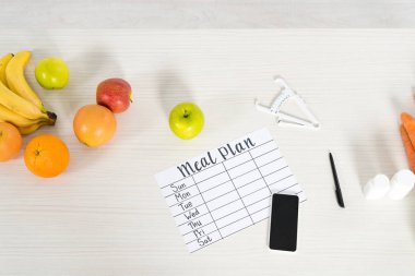 yemek planı üst görünümü, boş ekranlı akıllı telefon, kaliper, haplar ve ahşap yüzeyde taze meyveler