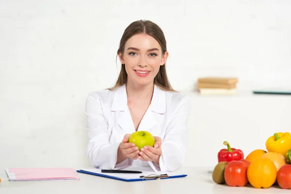 Vista Frontal Dietista Sonriente Con Capa Blanca Sosteniendo Manzana Lugar — Foto de Stock