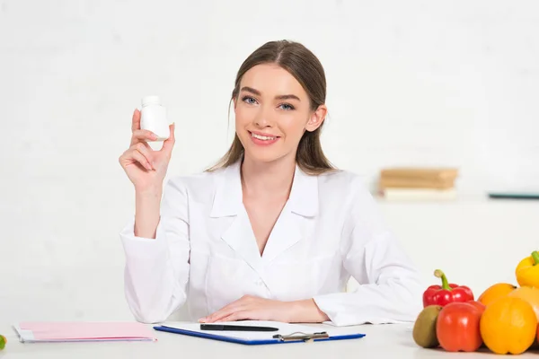 Smiling Dietitian White Coat Holding Pills Workplace Fruits Vegetables Table — Stock Photo, Image