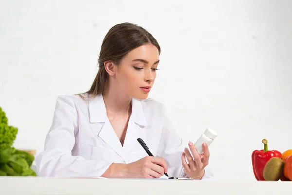 Dietista Concentrato Camice Bianco Con Pillole Scrittura Sul Posto Lavoro — Foto Stock